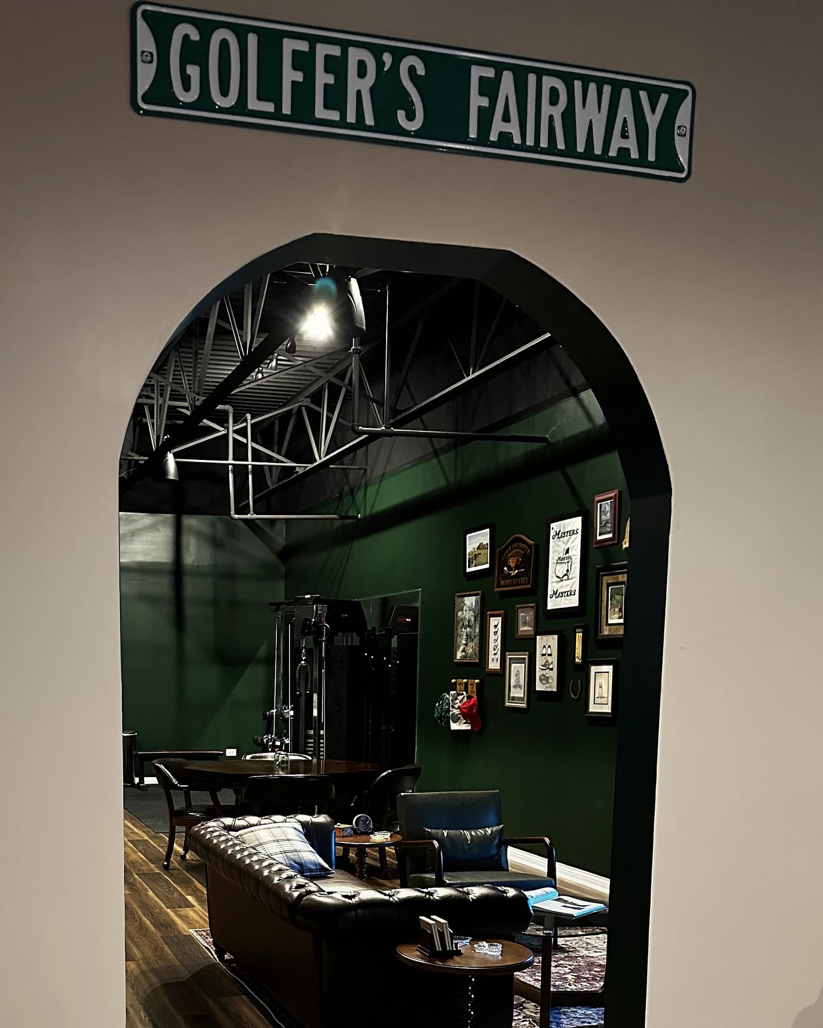 Archway into the lounge at That Golf Place: chesterfield sofa, gallery wall, and warm wood floors framed beneath a vintage 'Golfer's Fairway' street sign
