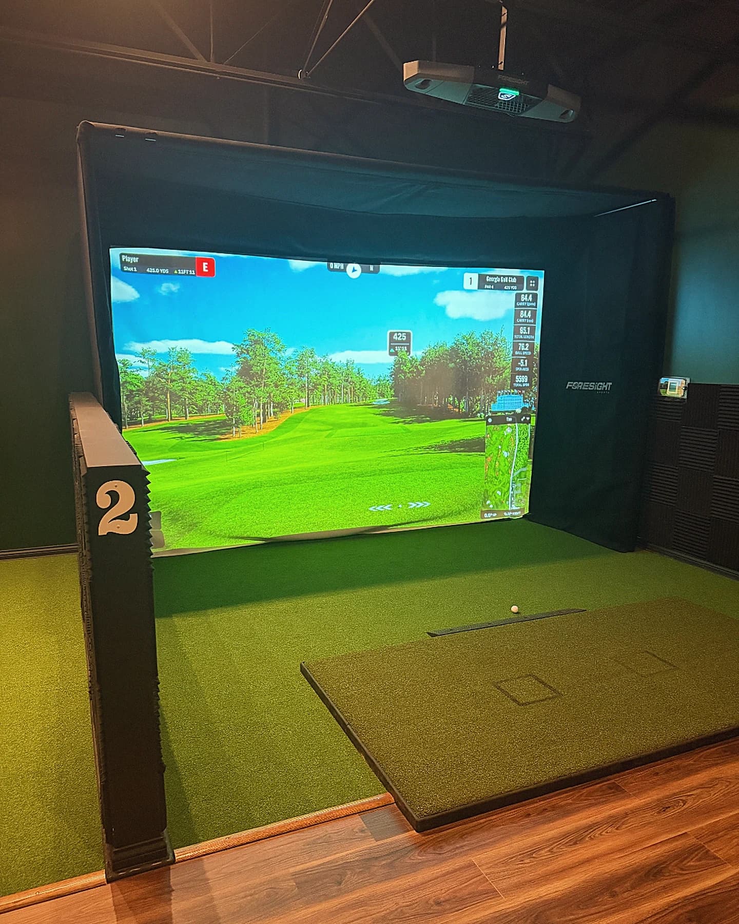Simulator bay 2 at That Golf Place with the GSPro screen lit on a Georgia Golf Club course, Foresight projector overhead, hitting mat and turf