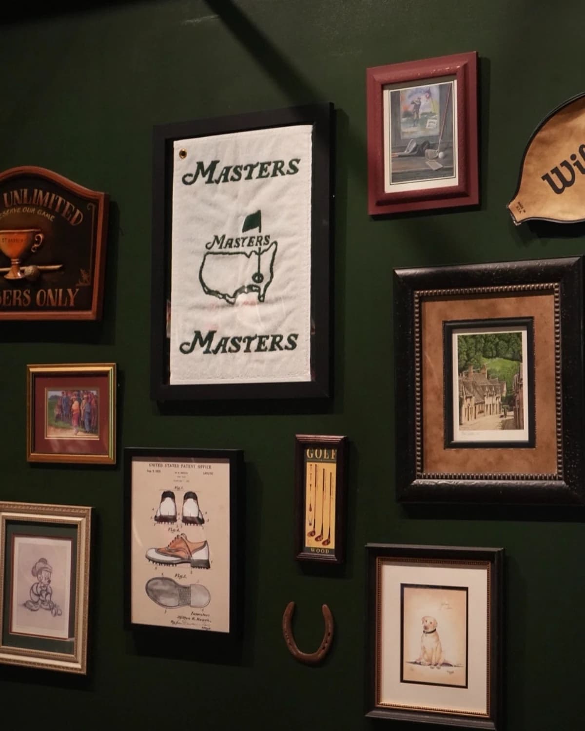 Gallery wall detail at That Golf Place with framed Masters flag, vintage golf shoe patent, horseshoe, and Labrador print on dark green panelling