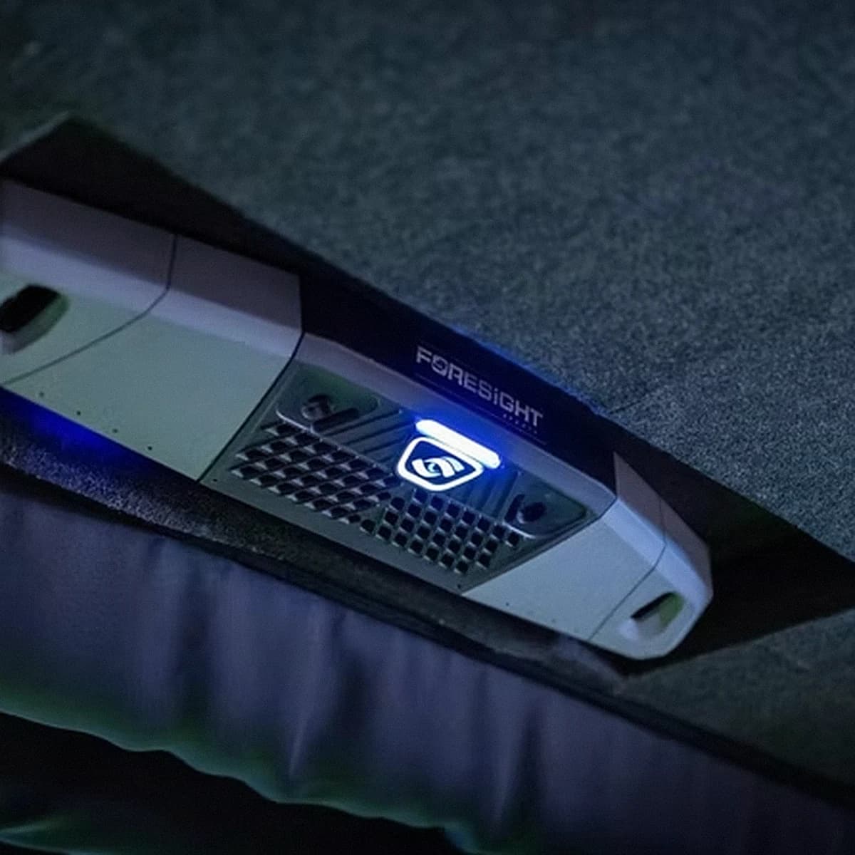 Close-up of a Foresight Sports launch monitor on the bay floor at That Golf Place, glowing with a blue indicator light and the Foresight logo, set against a textured turf hitting mat.
